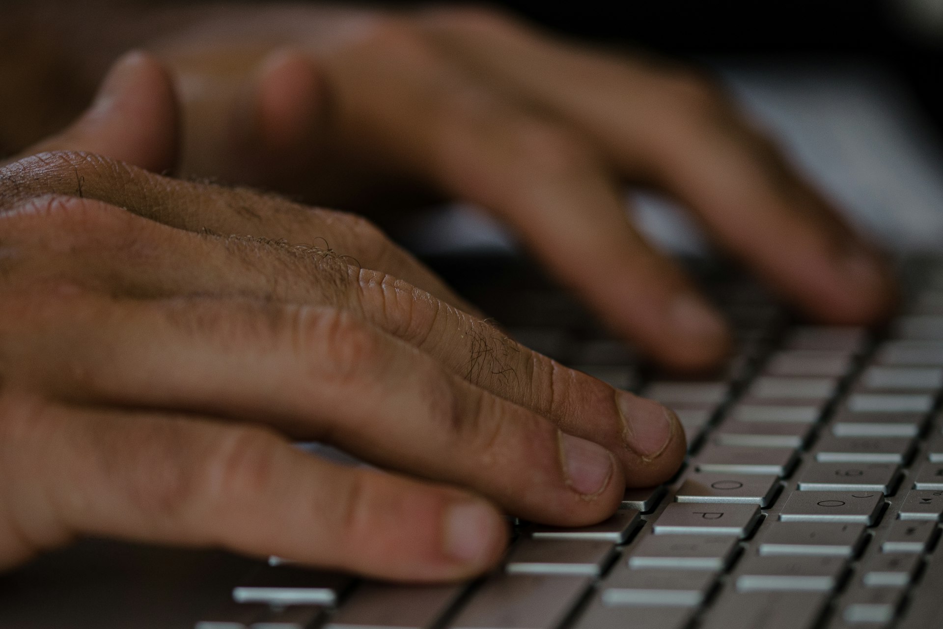 A close-up of hands typing on a keyboard with data visualizations on a monitor.